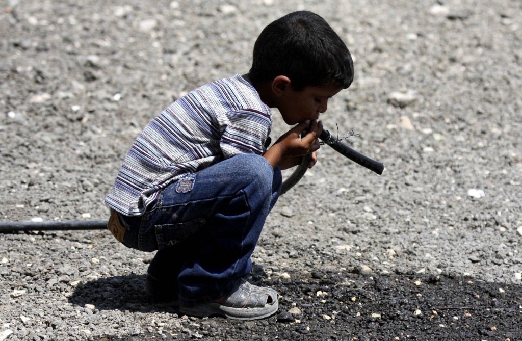 A Palestinian Bedouin child drinks water from a pipe near his tent on the road between Jericho and Ramallah